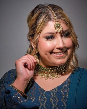 Portrait wearing traditional South Asian jewelry and formal attire against grey background.