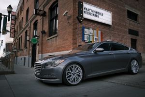Grey Genesis luxury sedan parked on urban street near brick building.