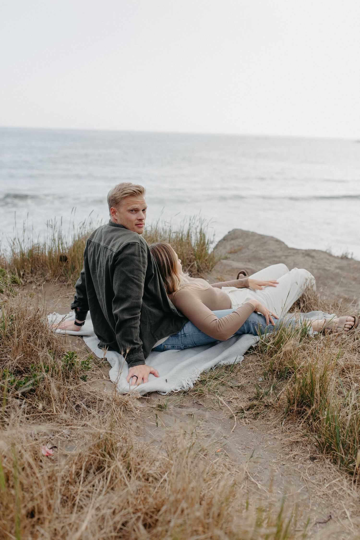 A couple relaxes on a blanket overlooking the ocean on a cloudy coastal afternoon.