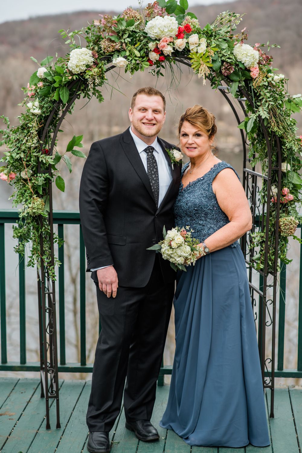 Couple stands under an elaborate floral wedding arch on an outdoor deck.