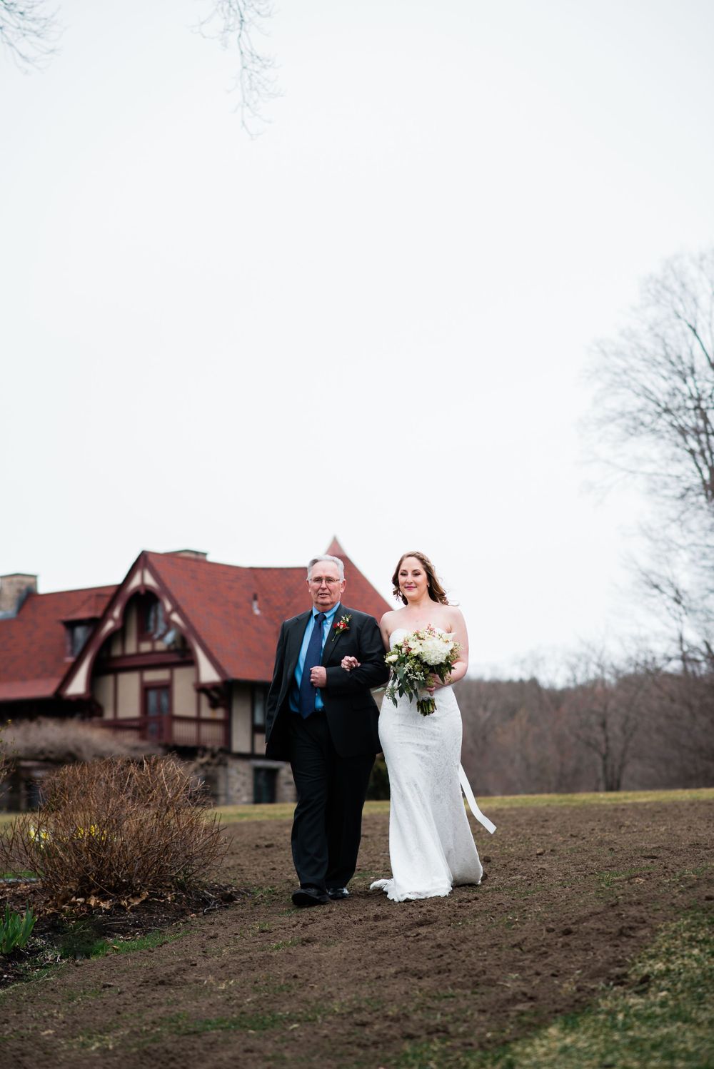 Wedding processional walking path leads to Tudor-style mansion with red roof.