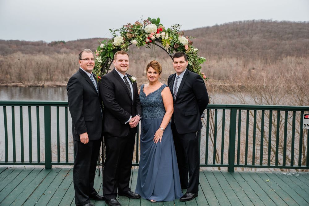Wedding party poses together under a floral arch on a deck with lake views.