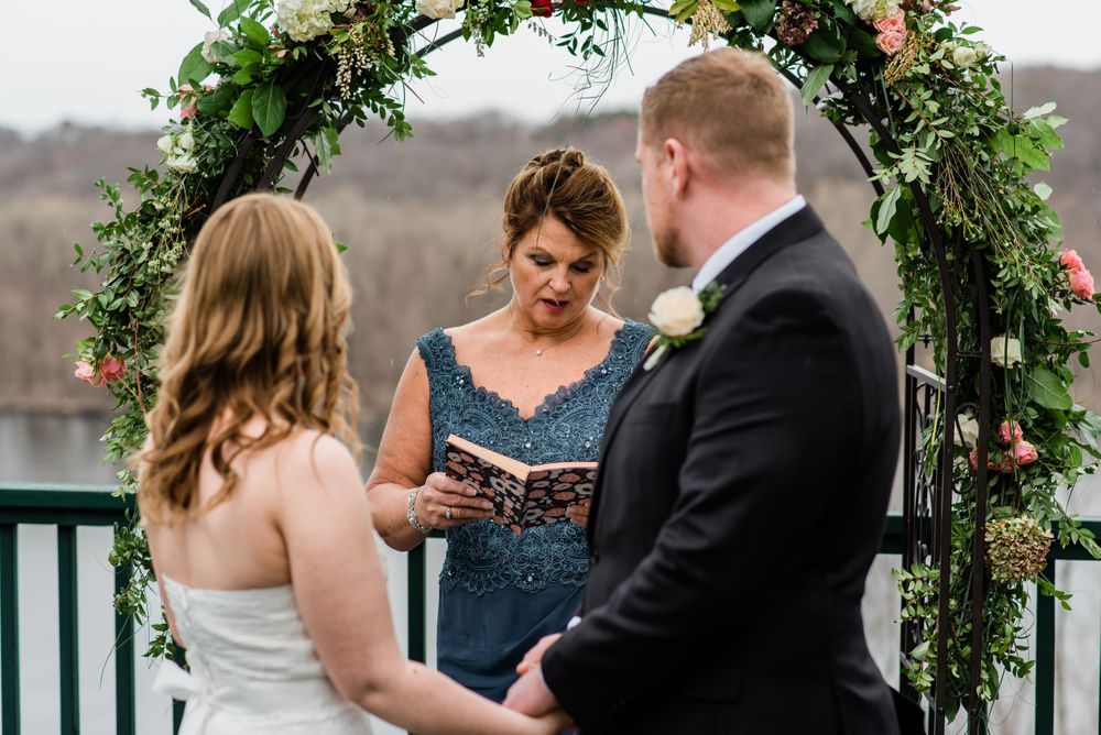 An intimate wedding ceremony under a flower-adorned arch with the officiant reading from a book.
