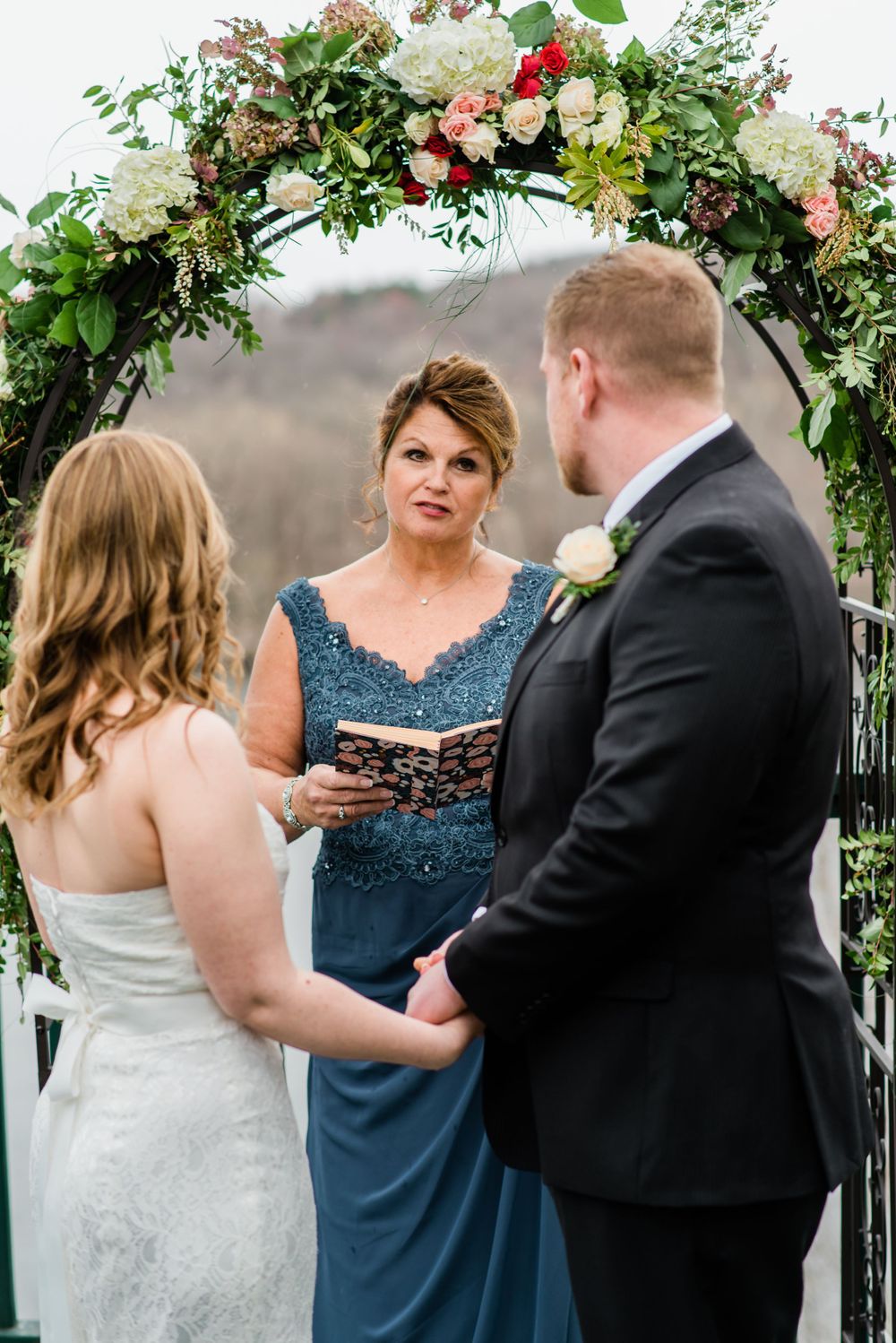An outdoor wedding ceremony featuring an elegant floral arch and lake backdrop.