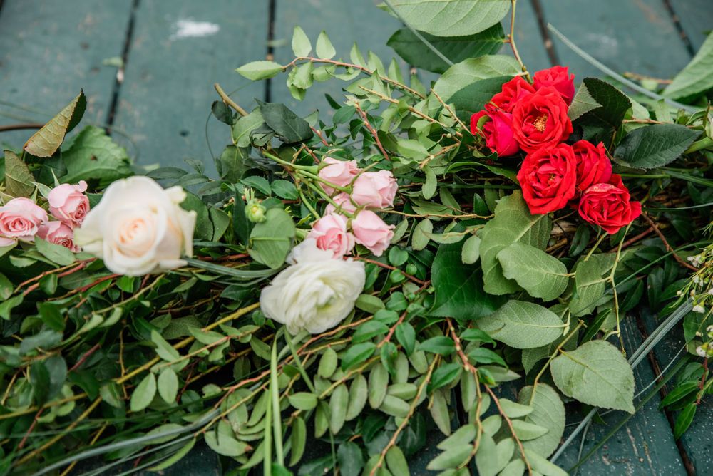 Fresh red and pink roses with green leaves arranged on a teal wooden surface.