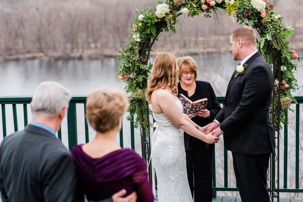 A winter wedding ceremony on a deck with guests watching the exchange of vows under a floral arch.