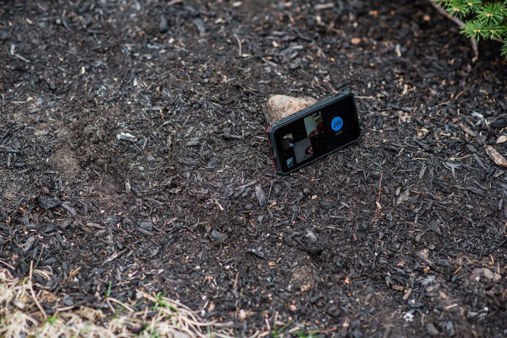 A smartphone lies on dark mulch or soil during an outdoor event.