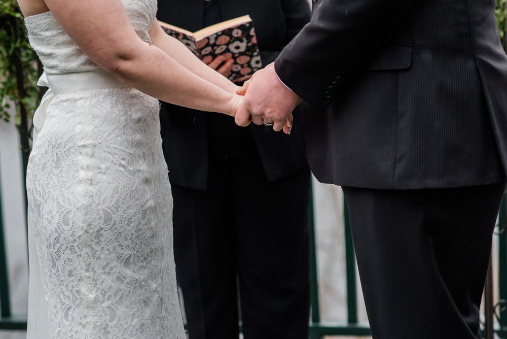 Close-up of hands holding during an outdoor wedding ceremony on a deck.