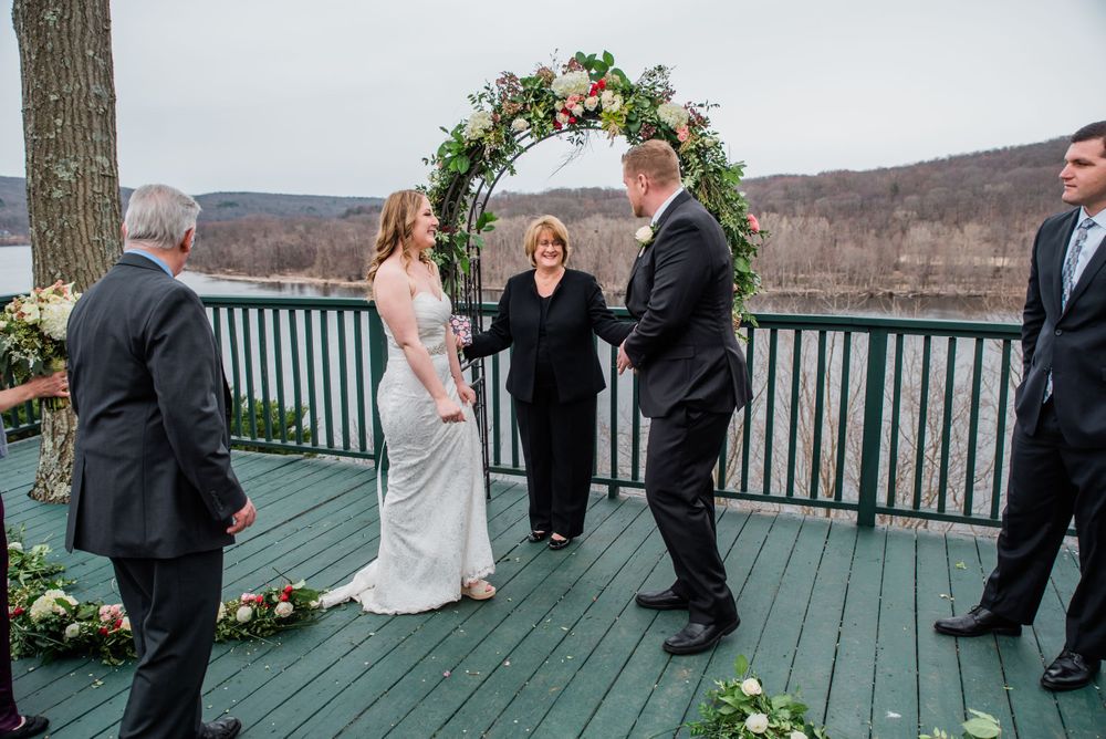 A wedding ceremony in progress on a green deck overlooking a lake with mountains in the background.