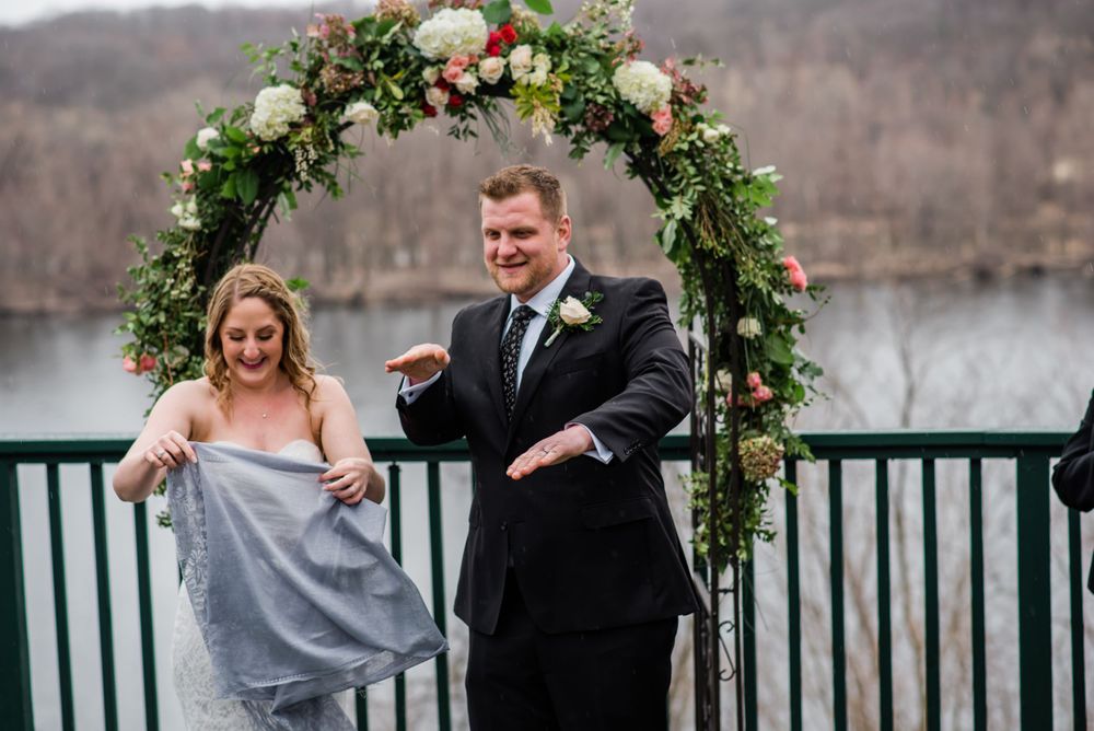 A couple celebrates joyfully under a floral arch during their lakeside deck wedding.