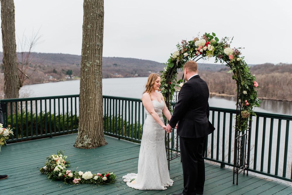 An intimate wedding ceremony unfolds on a scenic deck with a floral arch and lake view.