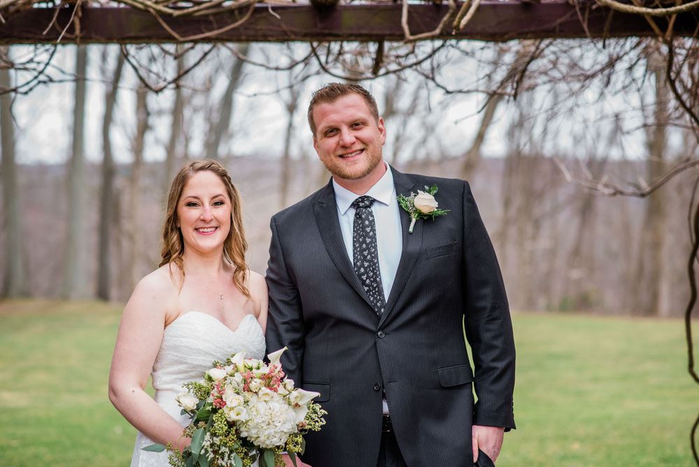A newlywed couple poses outdoors with a winter landscape behind them.