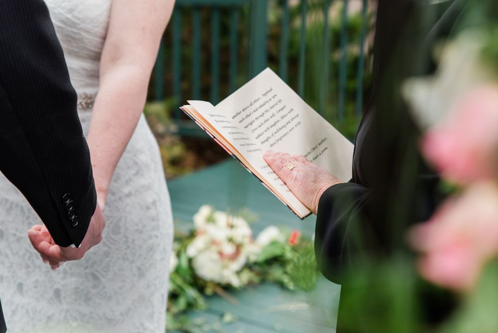 Close-up of hands and a ceremony book during an outdoor wedding service.