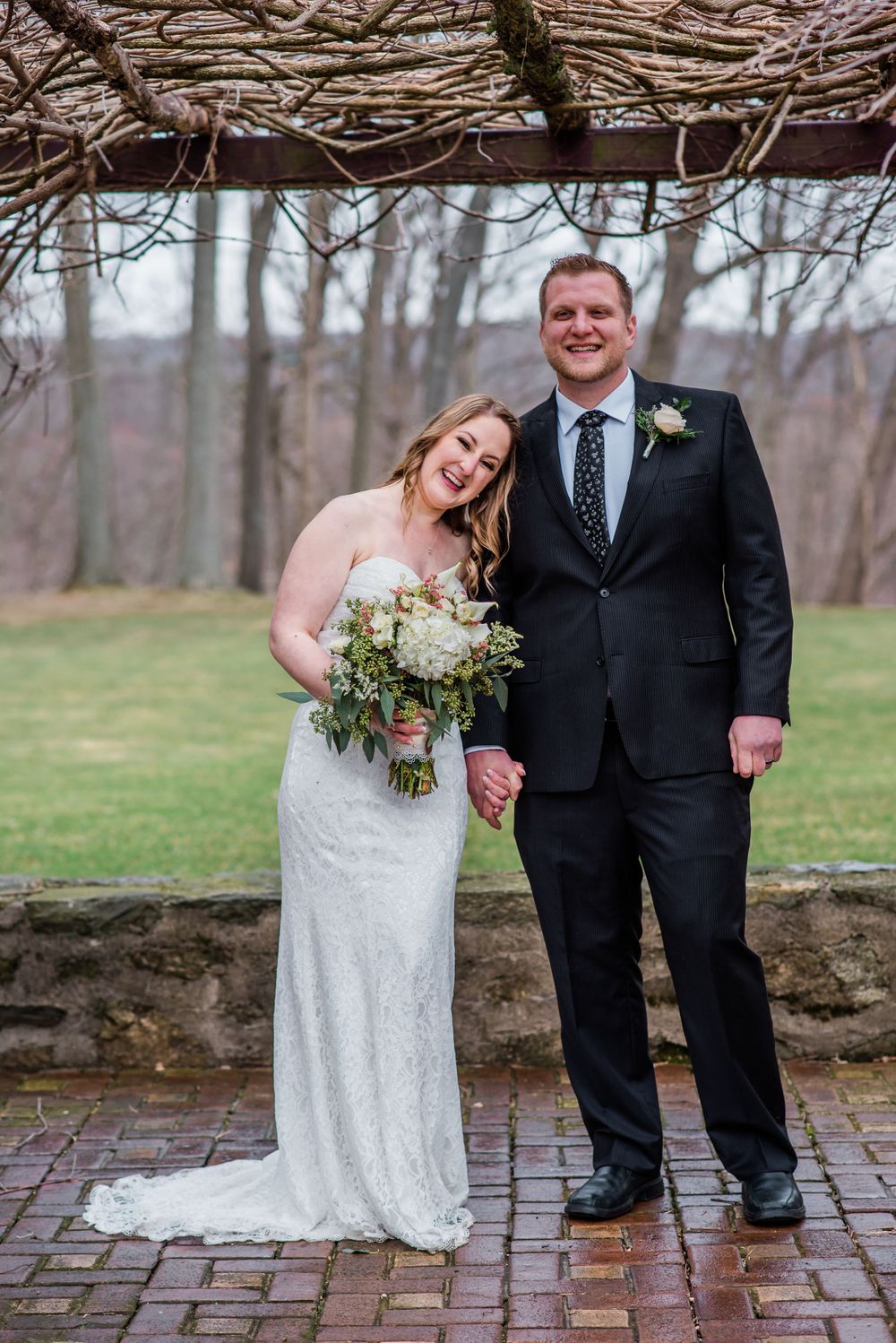A joyful newlywed couple poses under a rustic arbor with winter scenery.