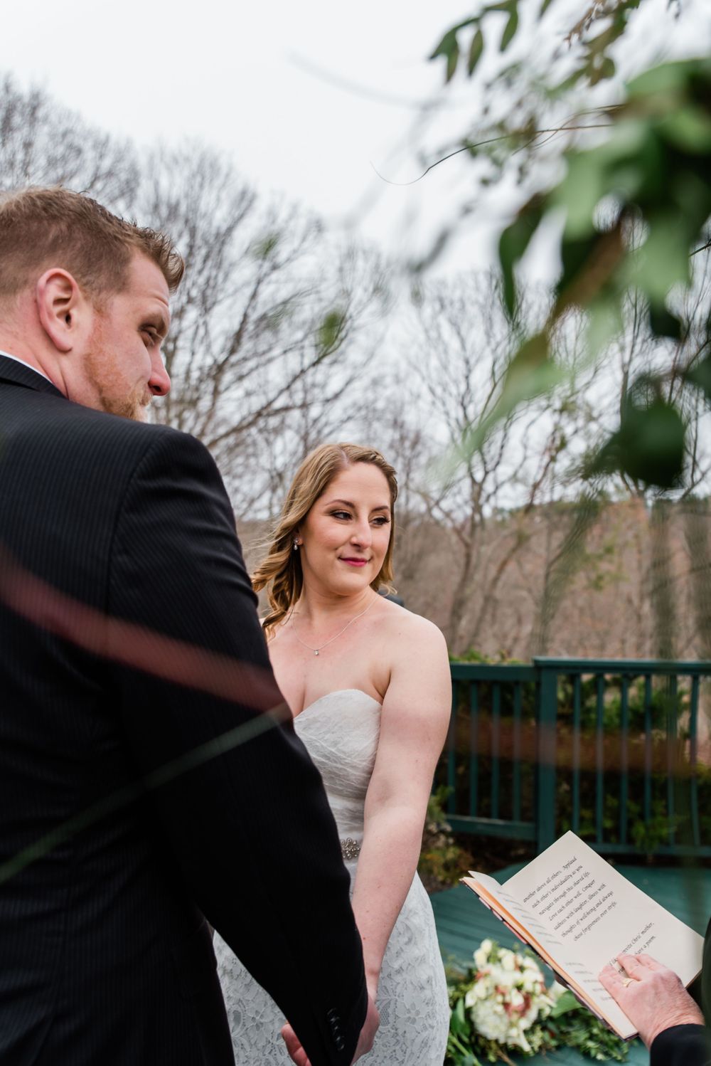 A couple exchanges vows during their outdoor deck ceremony with natural foliage framing the scene.