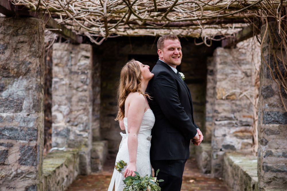 A couple shares a playful moment in front of a rustic stone structure.
