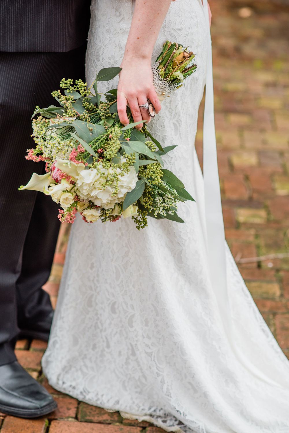 Close-up of a bridal bouquet with greenery and delicate florals against a lace wedding dress.