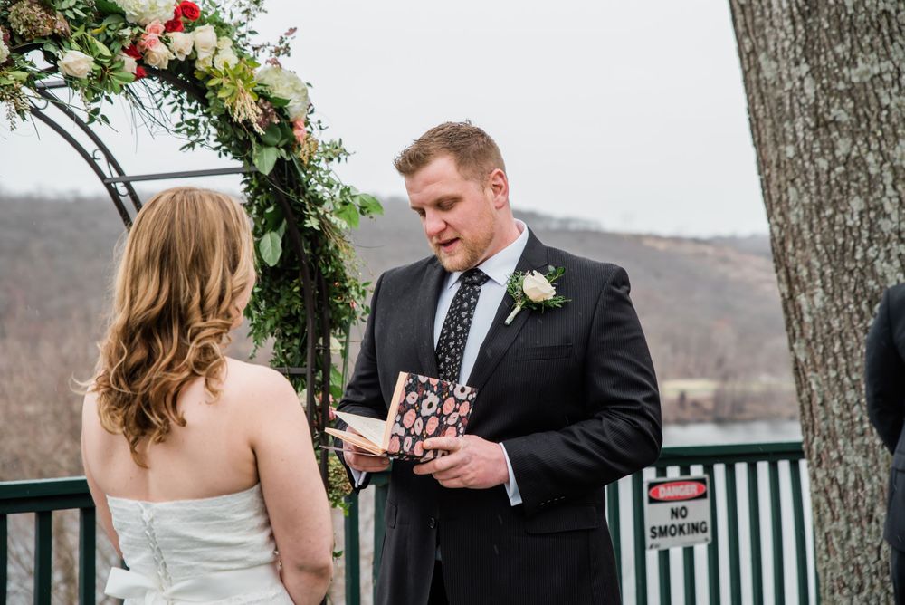 A wedding ceremony moment under a floral arch with mountains in the background.