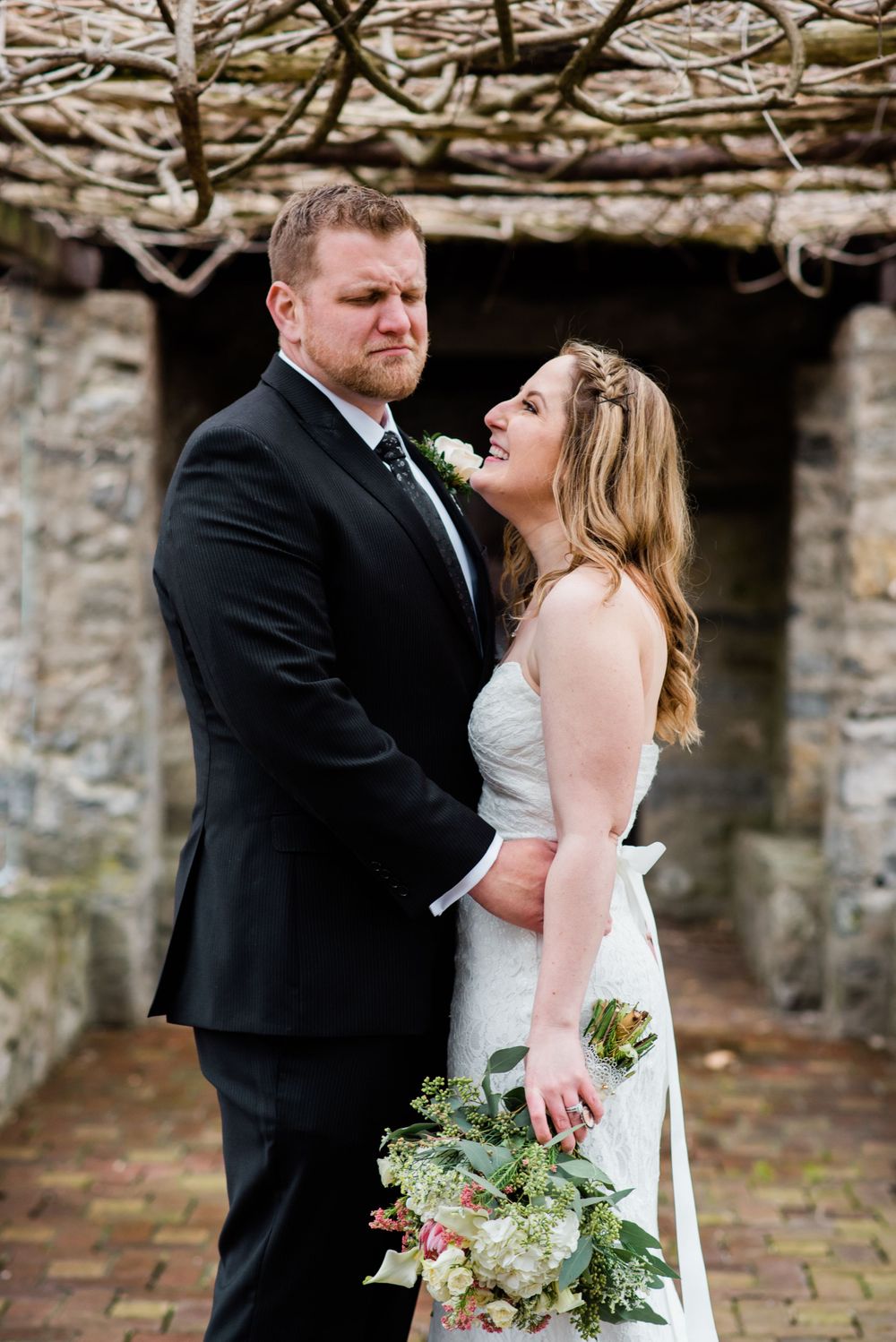 A romantic wedding portrait of a couple standing in a stone archway with a lush floral bouquet.