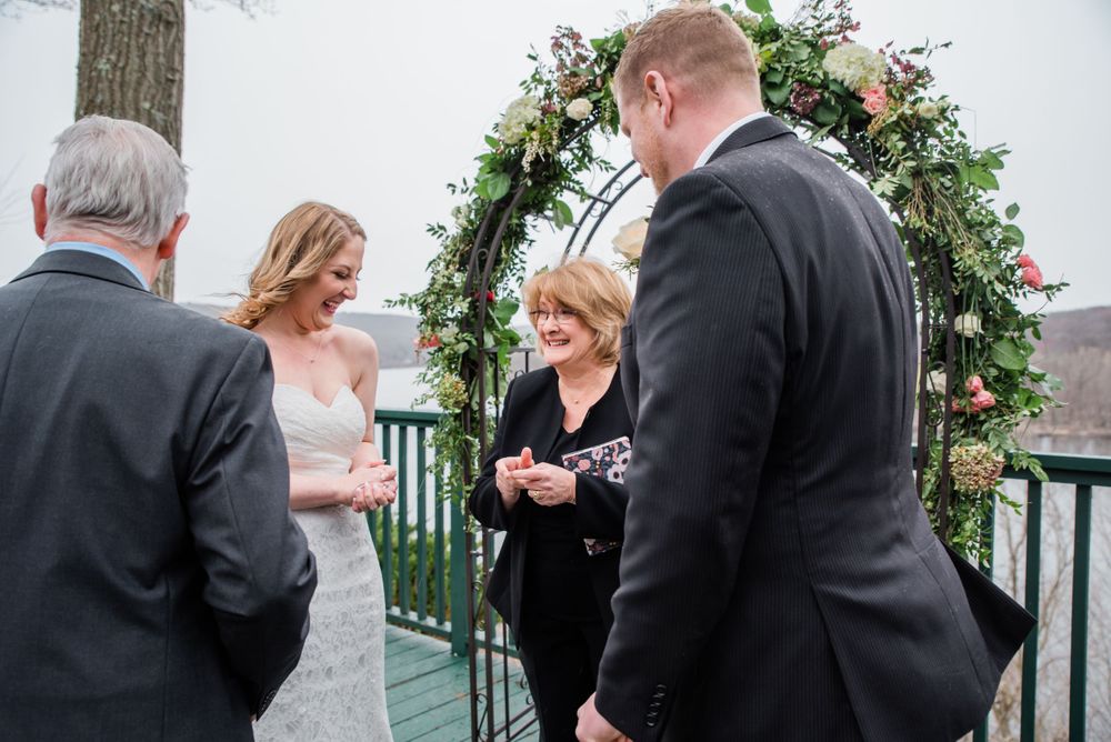 Wedding ceremony participants gather on outdoor deck during ring exchange.