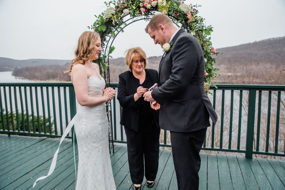 Wedding ceremony on deck with floral arch and mountain backdrop.