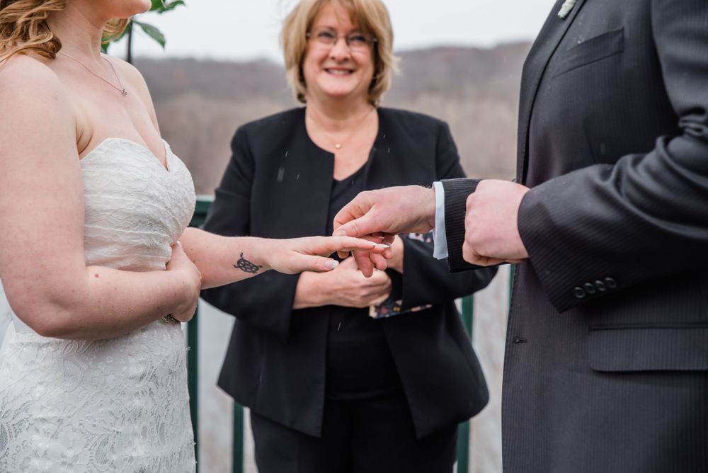 Exchange of wedding rings during an outdoor ceremony led by an officiant in black.