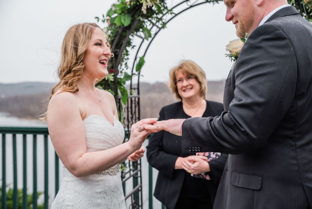 Happy couple exchanges rings during outdoor ceremony with officiant present.