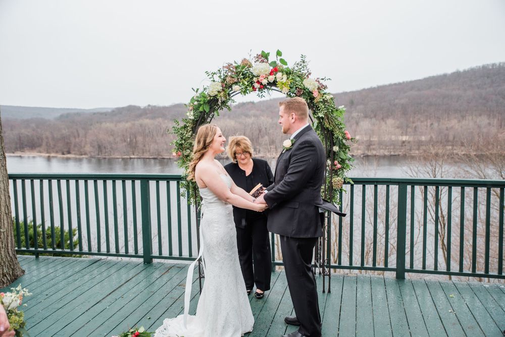 Wedding ceremony beneath floral arch overlooking scenic winter landscape.