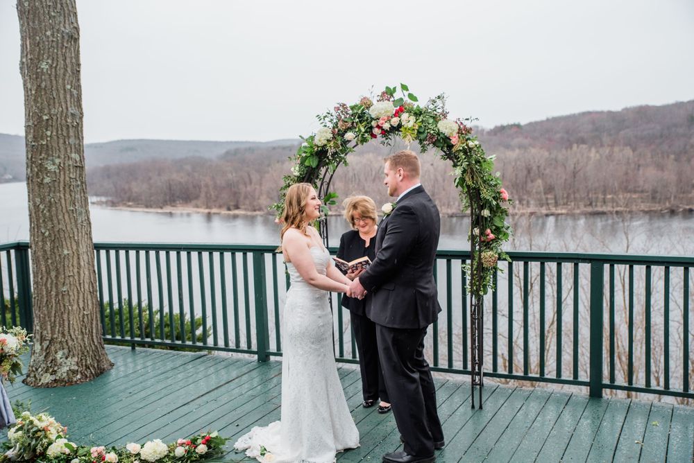 Intimate wedding ceremony under floral arch on deck overlooking lake and mountains.