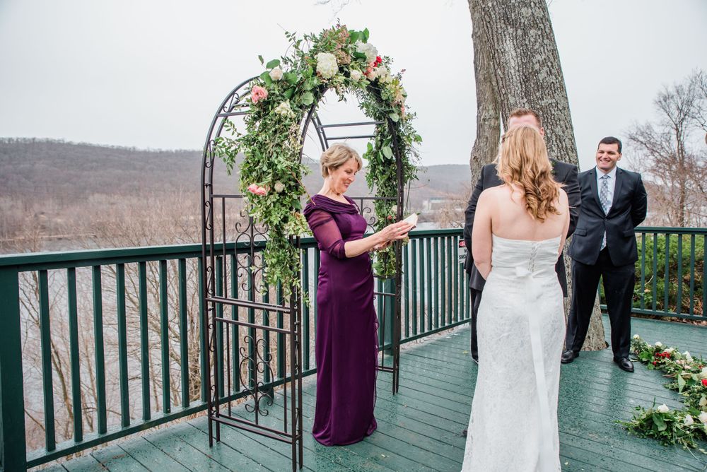 Outdoor wedding ceremony on deck with floral arch and winter landscape views.