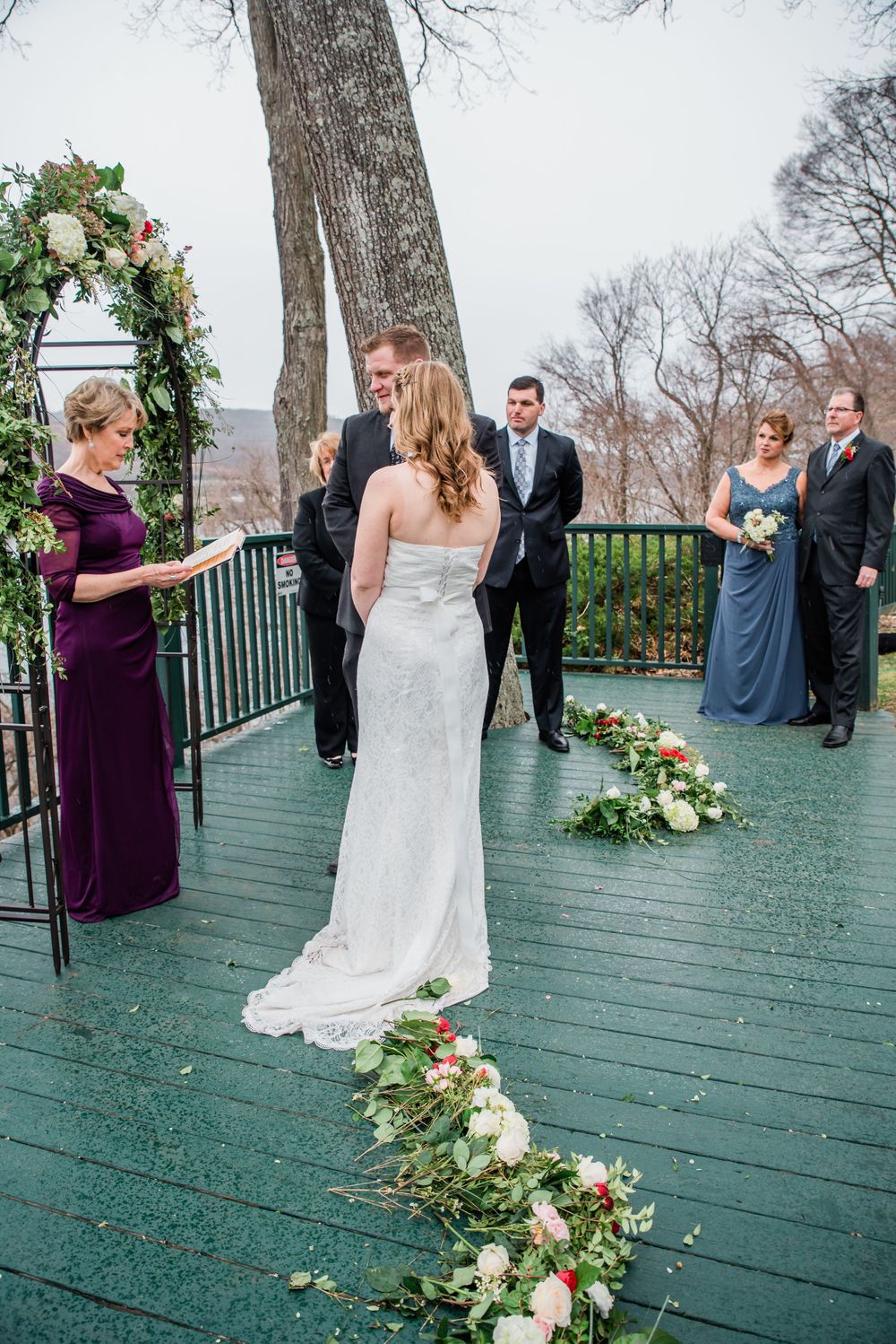Wedding ceremony on green deck with floral decorations and lake view backdrop.