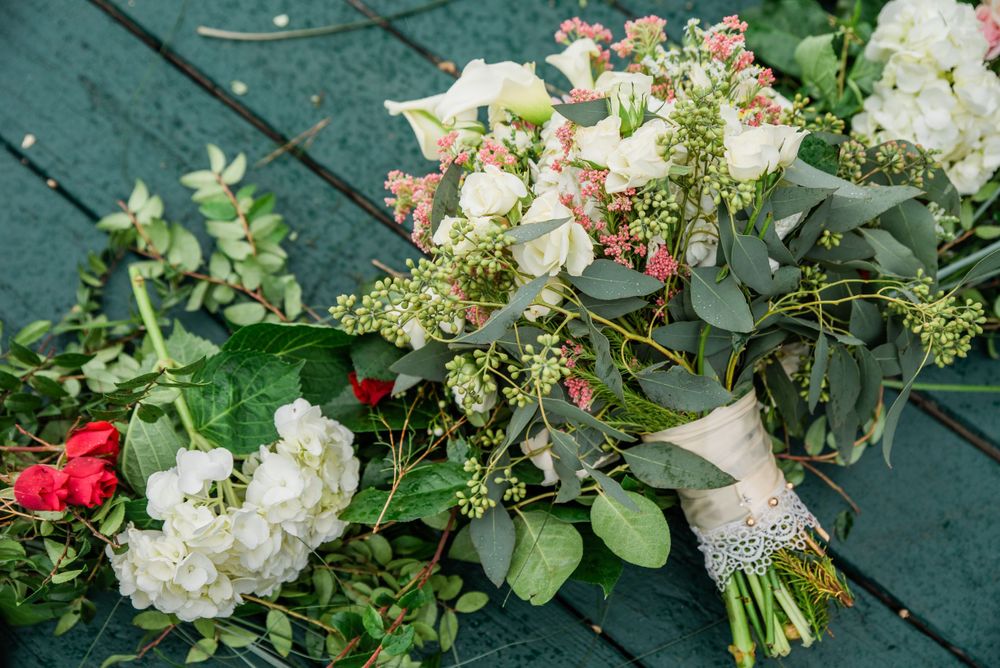 Wedding bouquet with white roses, greenery and pink flowers laying on teal deck.