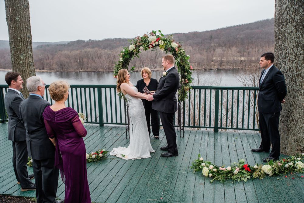Wedding ceremony under floral arch on lakeside deck during winter.