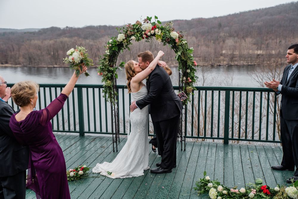 Wedding celebration under floral arch with lake and mountain backdrop.