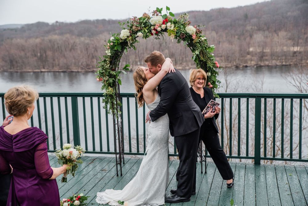 Romantic ceremony moment under floral arch with lake view in background.