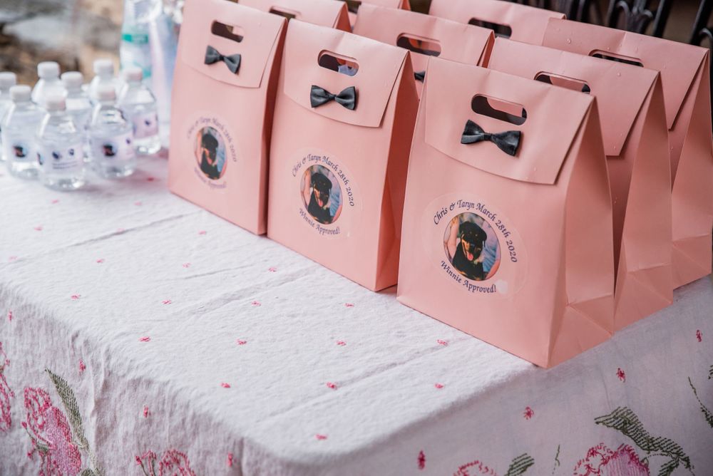 Pink favor boxes decorated with bow ties and monograms arranged on a white tablecloth.