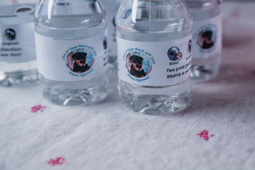 Custom labeled water bottles with monogram designs arranged on a pink and white tablecloth.