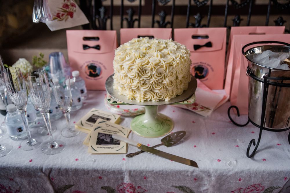 An elegant white wedding cake with textured frosting displayed on a dessert table with pink favor boxes.