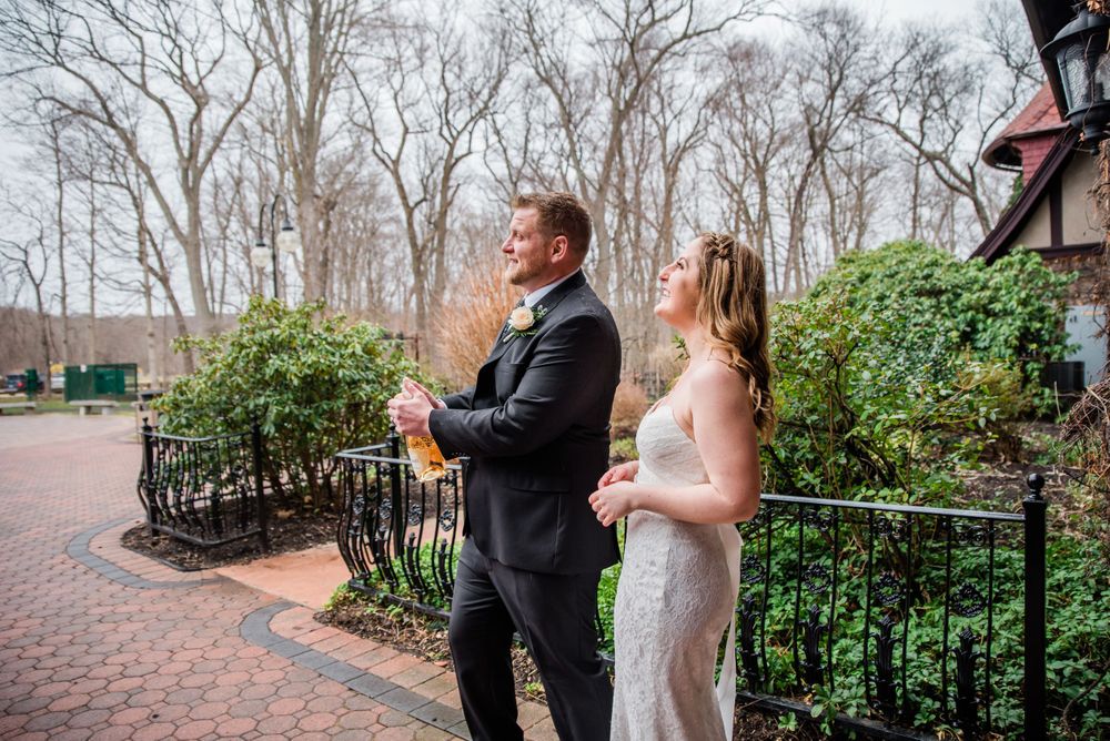 A couple enjoys drinks on an outdoor brick patio surrounded by early spring greenery.