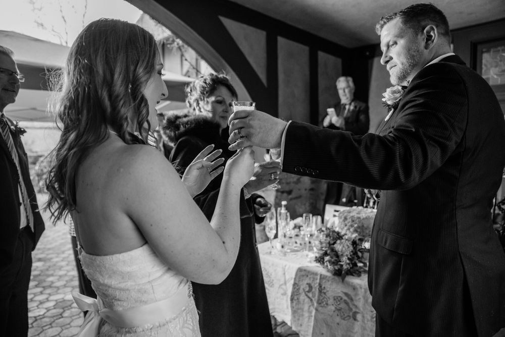 A black and white photo of a couple toasting with champagne glasses at their wedding reception.
