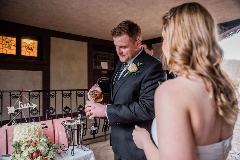 A couple sharing drinks and smiles at their wedding reception near decorative windows.