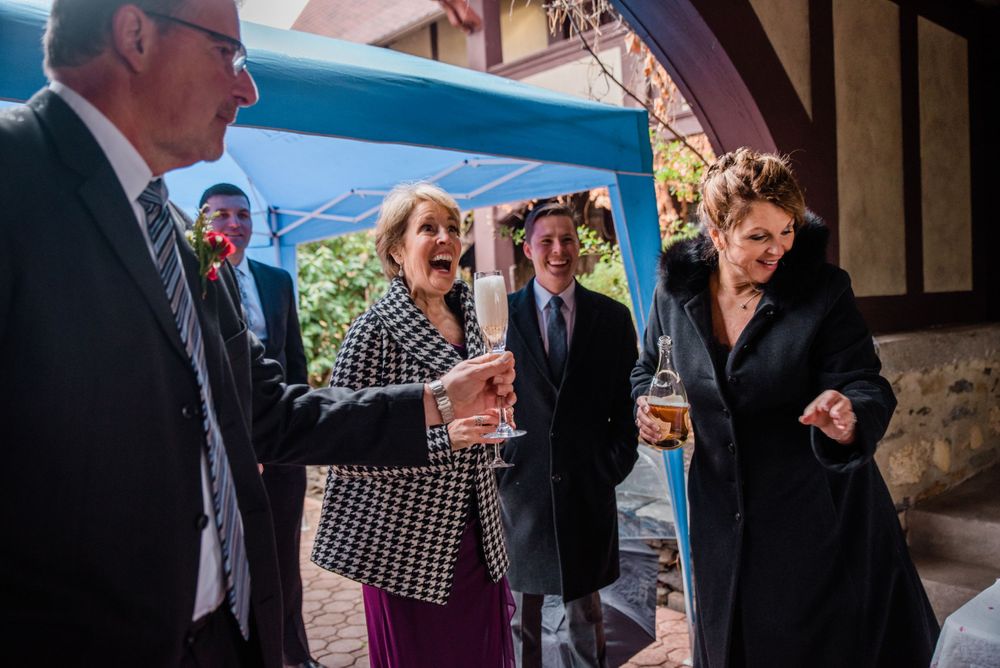Wedding guests enjoy drinks and conversation under an archway during a reception.