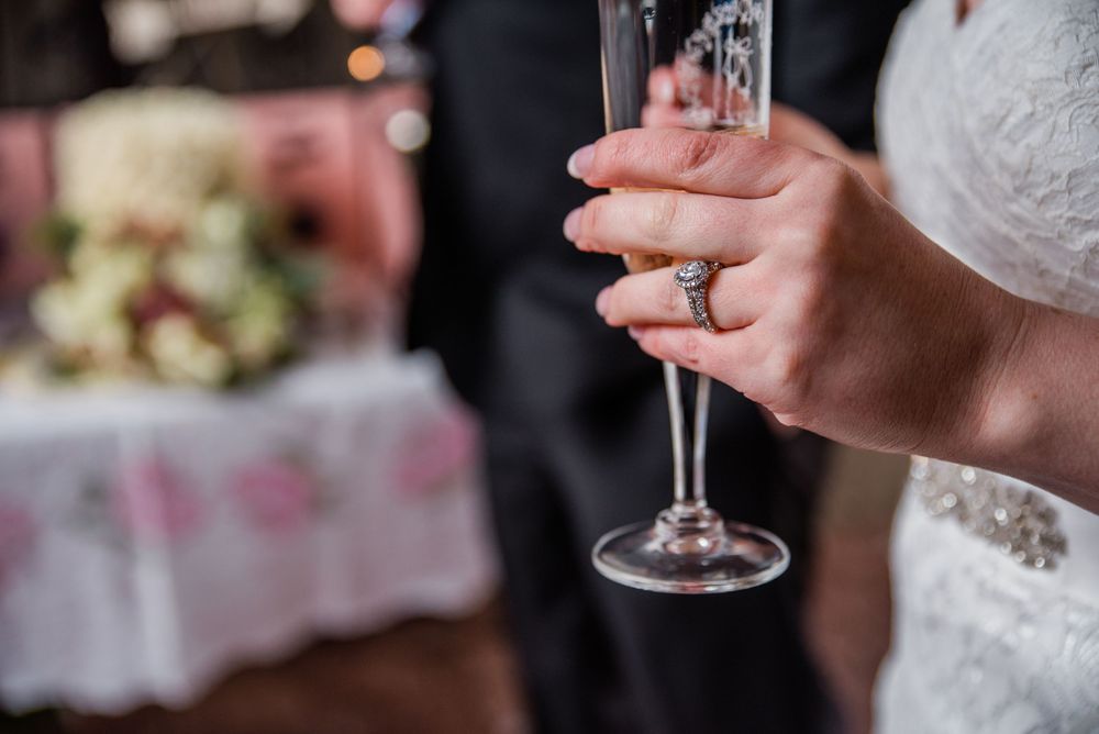 Close-up of a wedding ring and champagne glass held by someone in a white dress.