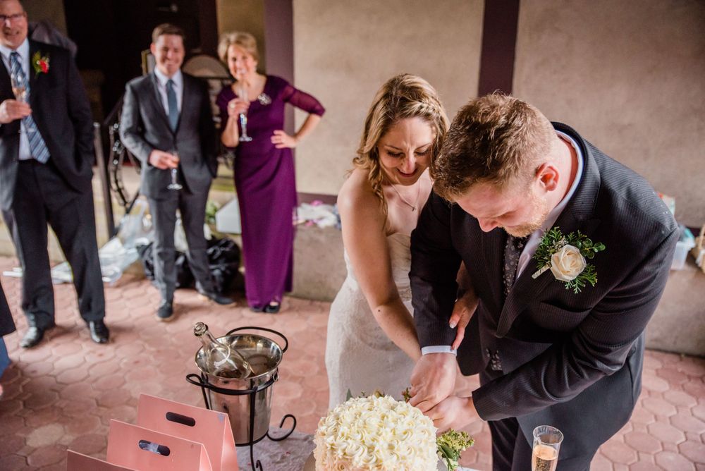 Couple cutting their white wedding cake while guests watch in the background.