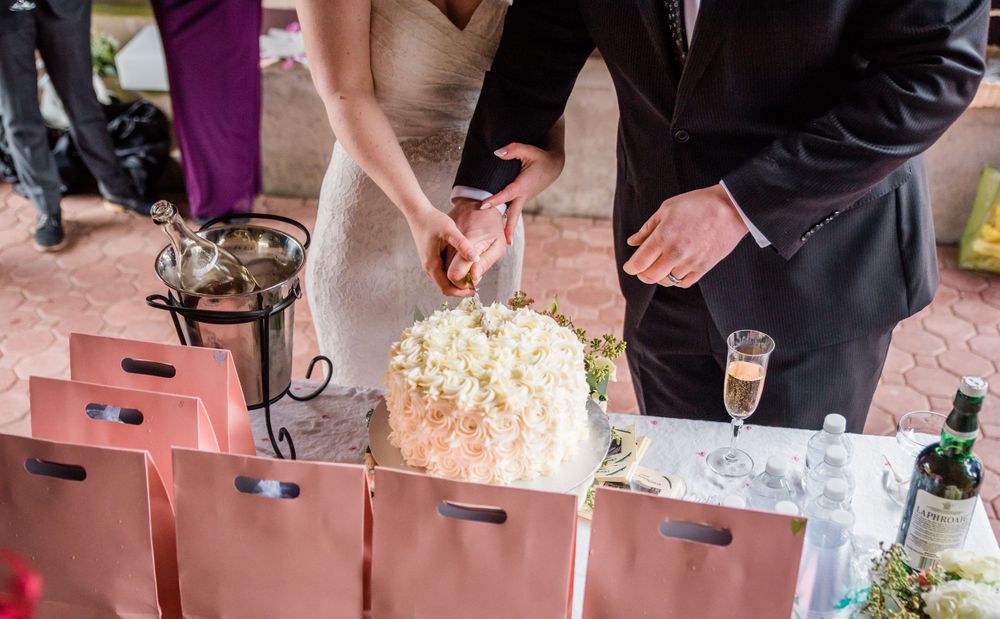 Newlyweds slice into their elegant white wedding cake at the reception.