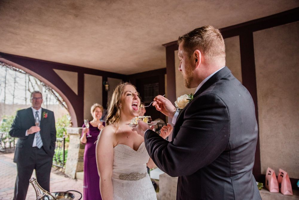 A couple shares a playful moment with cake during their wedding reception while guests watch.