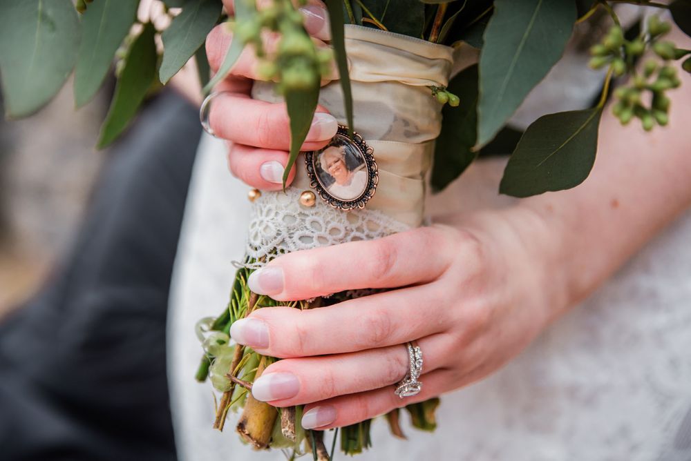 Close-up of hands holding a wedding bouquet with rings and greenery.
