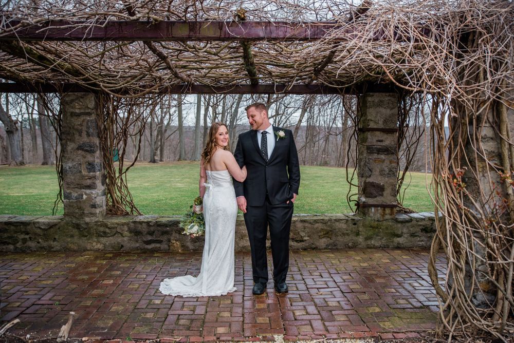 A couple shares an intimate moment under a rustic stone pergola with winter vines.