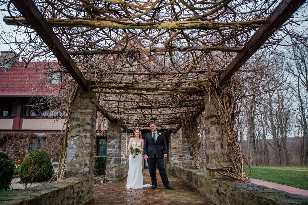 Wedding couple photographed under a long stone pergola with climbing vines.