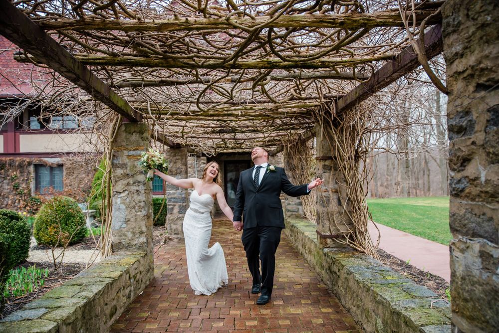 A couple walks hand in hand through a vine-covered stone pergola.